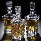 Trois carafes à whisky en cristal aux designs différents, remplies d'alcool ambré, posées sur fond noir avec reflets dorés.