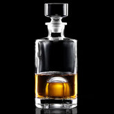 Carafe à whisky ronde en verre transparent remplie de whisky ambré, photographiée sur fond noir avec bouchon en verre biseauté.