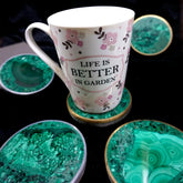 Tasse à motifs floraux posée sur un dessous de verre en malachite verte cerclé, entourée d'autres exemplaires sur fond noir