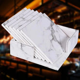 Lot de 6 dessous de verre effet marbre disposés en éventail devant leur boîte de rangement, dans une ambiance de bar.