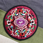 Dessous de verre en tissu brodé rouge bordeaux avec motif floral doré vu en gros plan.