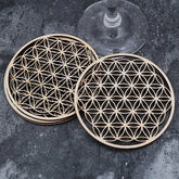 Lot de cinq sous-verres en bois motif Fleur de Vie empilés, avec un verre à pied posé sur le dessus.