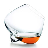 Verre à whisky à bascule rempli de whisky ambré, photographié en équilibre sur son point de bascule sur fond blanc.