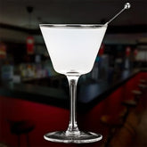 Verre à cocktail coupe vintage rempli d'un cocktail blanc avec pique à olive, dans une ambiance de bar aux tons rouges et noirs.