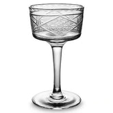 Verre à cocktail vide à motif géométrique en relief, photographié sur fond blanc.