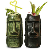 Duo de verres à cocktail Statue de l'Île de Pâques, l'un vert garni de menthe et paille cœur, l'autre noir garni d'aloe, sur fond blanc.