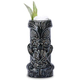 Verre à cocktail Tiki Dieu Noir rempli de glace pilée avec une garniture végétale sur fond blanc