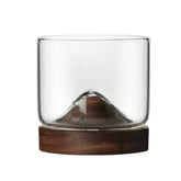 Verre à whisky avec socle en bois sculpté en forme de montagne, vide, présenté sur fond blanc