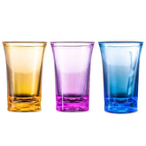 Trois verres à shot colorés (orange, violet et bleu) alignés sur fond blanc.