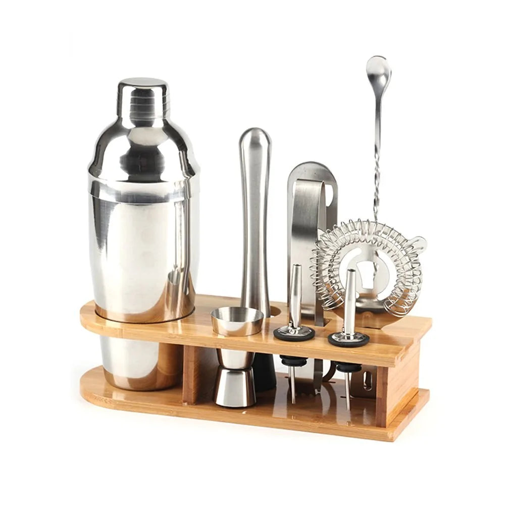 Kit cocktail complet avec shaker, doseur, pilon, pince et passoire sur son support en bambou, présenté sur fond blanc.
