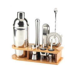 Kit cocktail complet avec shaker, doseur, pilon, pince et passoire sur son support en bambou, présenté sur fond blanc.