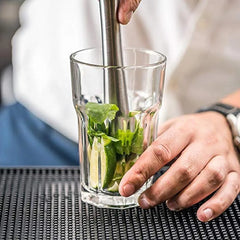 Utilisation du pilon du kit pour écraser de la menthe fraîche et du citron vert au fond d'un verre, préparation d'un mojito.