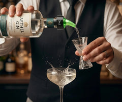 Barman versant du gin à l'aide du bec verseur 3 cl dans un verre doseur pour préparer un cocktail