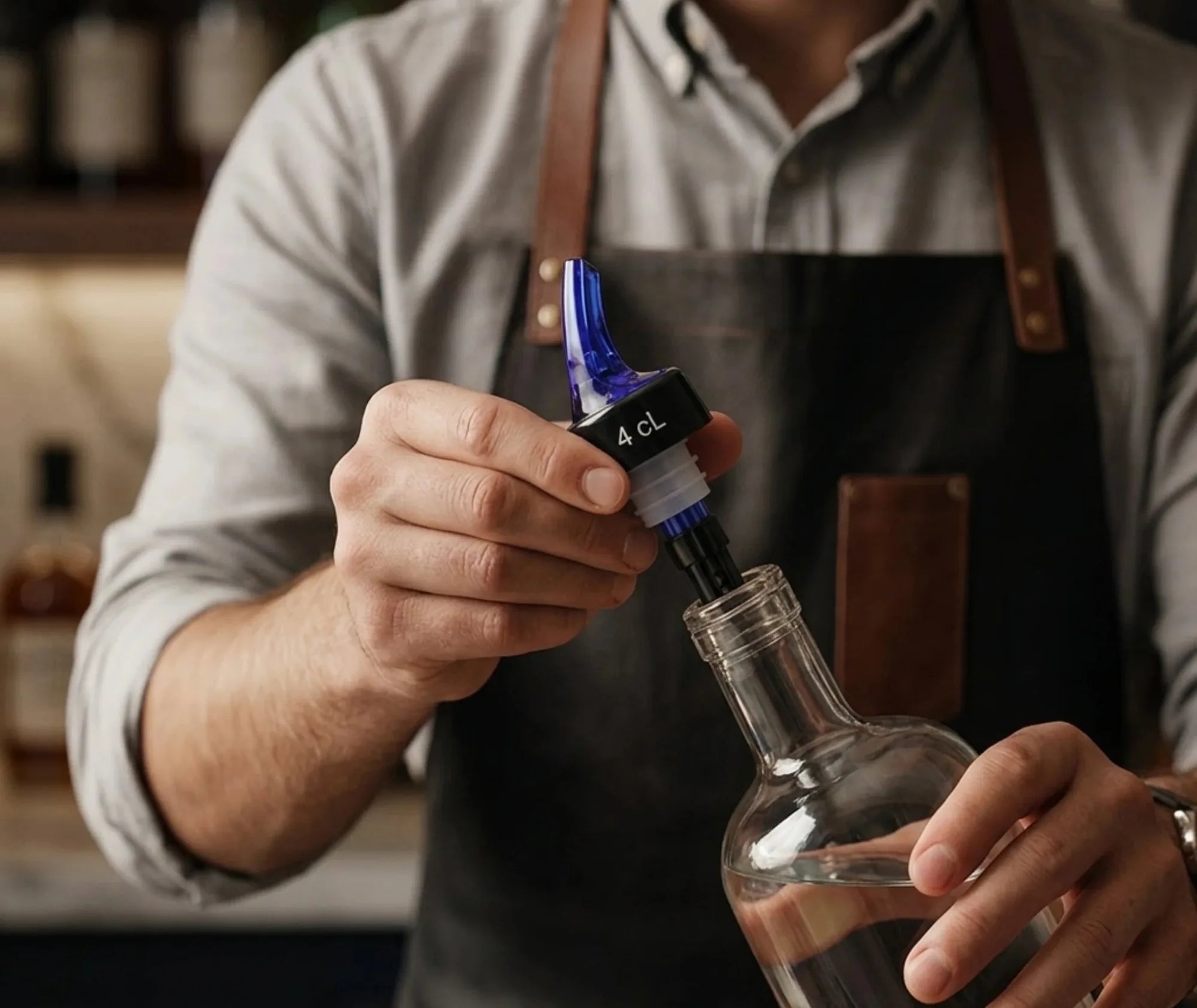 Gros plan sur les mains d'un barman insérant le bec verseur doseur 4 cl dans le goulot d'une carafe en verre.