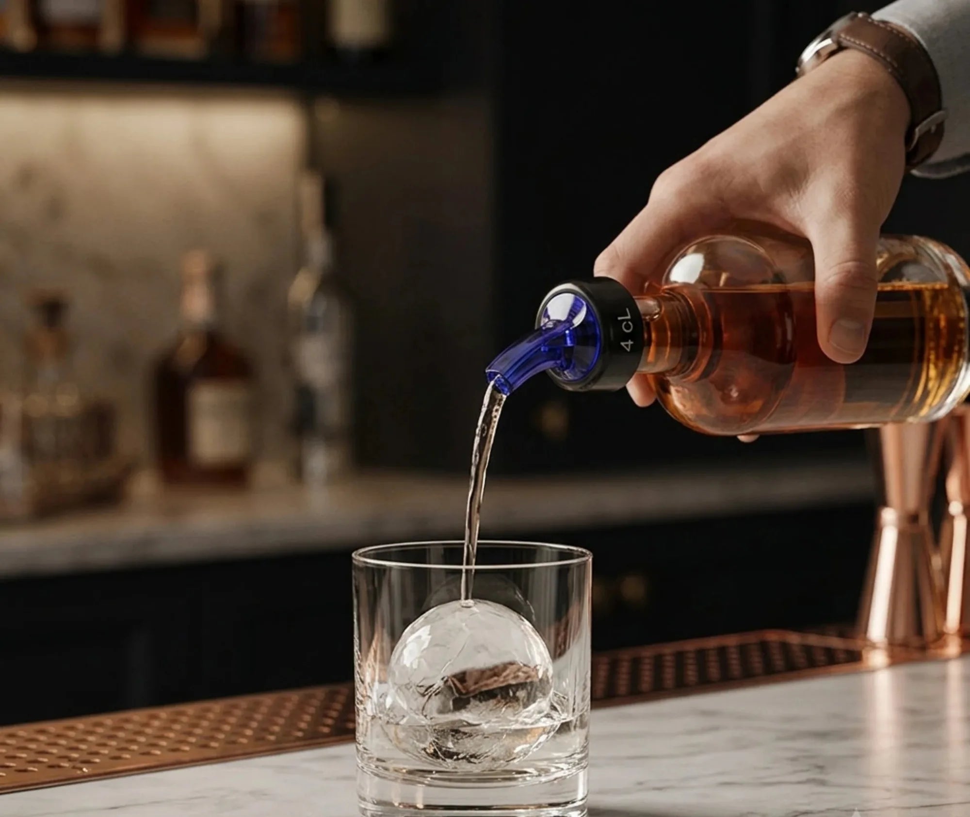 Un barman verse un spiritueux à travers le bec verseur 4 cl directement dans un verre à whisky contenant une boule de glace.