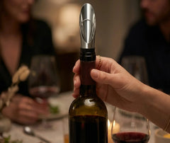 Une convive tient une bouteille de vin équipée du bec verseur anti-goutte lors d'un dîner entre amis.