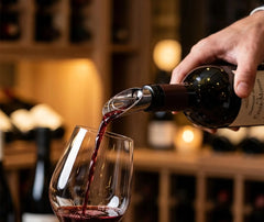 Une personne verse du vin rouge à l'aide du bec verseur anti-goutte dans une cave à vin élégante.