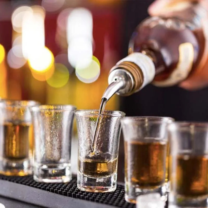 Barman utilisant un bec verseur pour servir des shots d'alcool ambré dans des verres alignés.