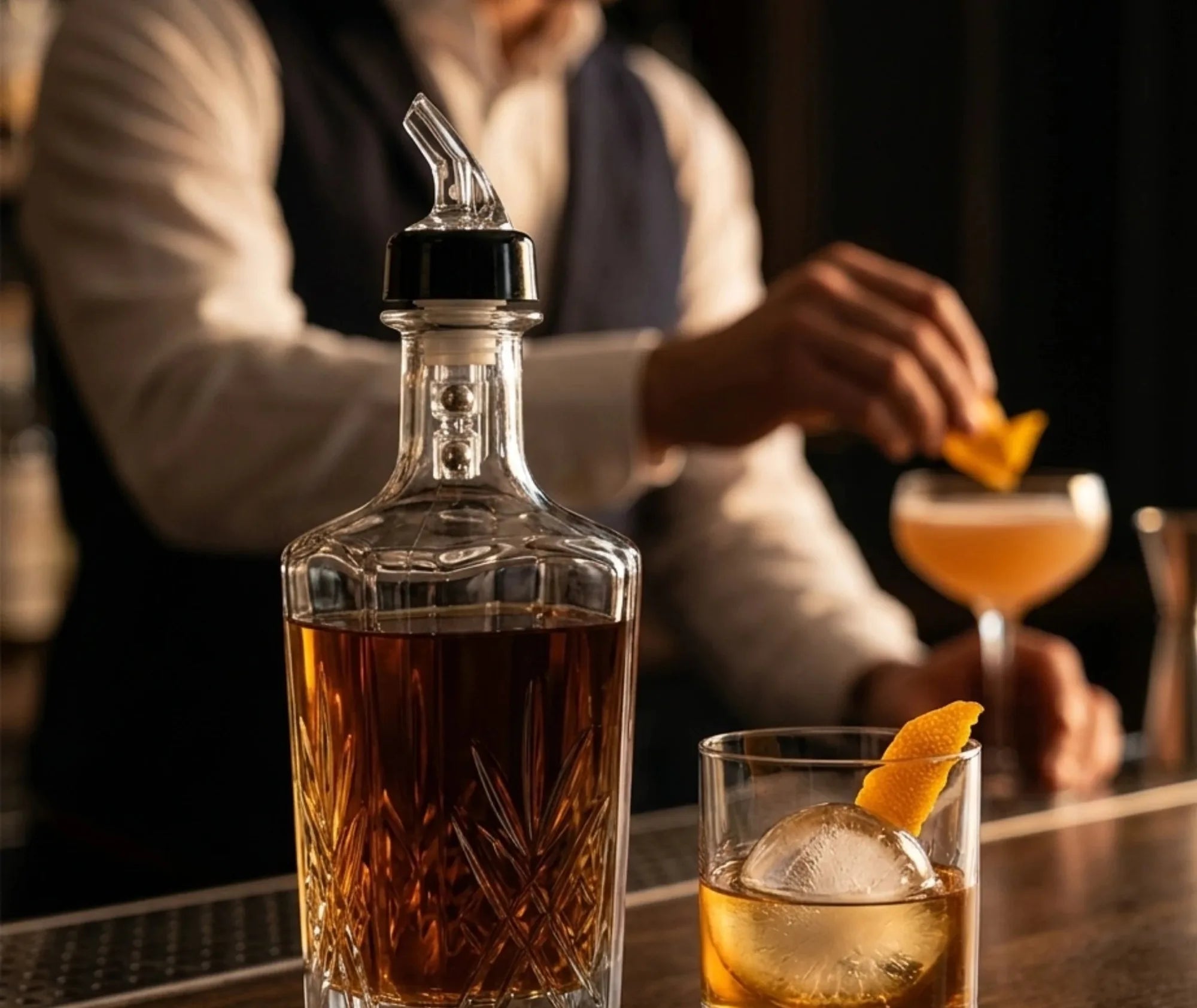 Bec verseur installé sur une carafe en cristal, avec un cocktail préparé au bar en arrière-plan.