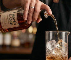 Bec verseur fixé sur une bouteille de bourbon Hearth & Oak, versé dans un verre à mélange rempli de glaçons.