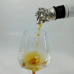 Bec verseur tête de lion argenté fixé sur une bouteille, versant une liqueur ambrée dans un verre facetté