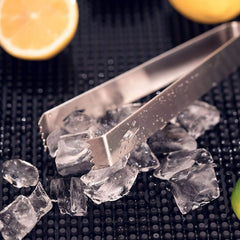 Gros plan sur la pince à glaçons du kit posée sur des glaçons avec des demi-citrons en arrière-plan