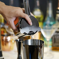 Gros plan sur la passoire à cocktail Hawthorne du kit versant une préparation dans un shaker noir