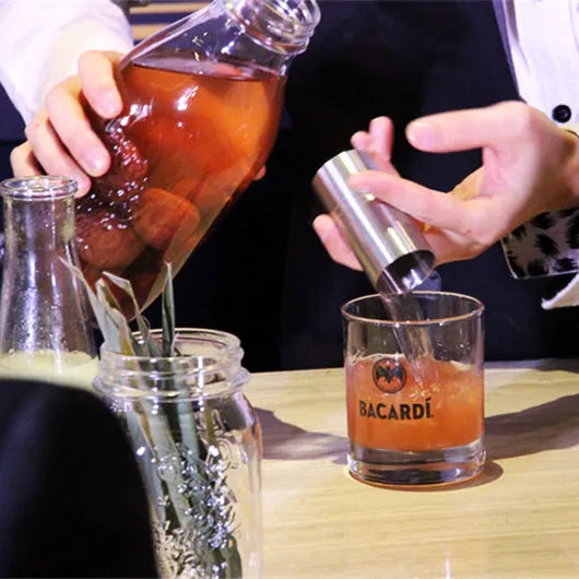 Doseur à cocktail versant un spiritueux ambré dans un verre Bacardi rempli de glaçons