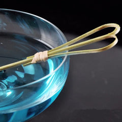Gros plan sur un pic à cocktail en bambou naturel posé sur le bord d'un bol contenant un liquide bleu turquoise.