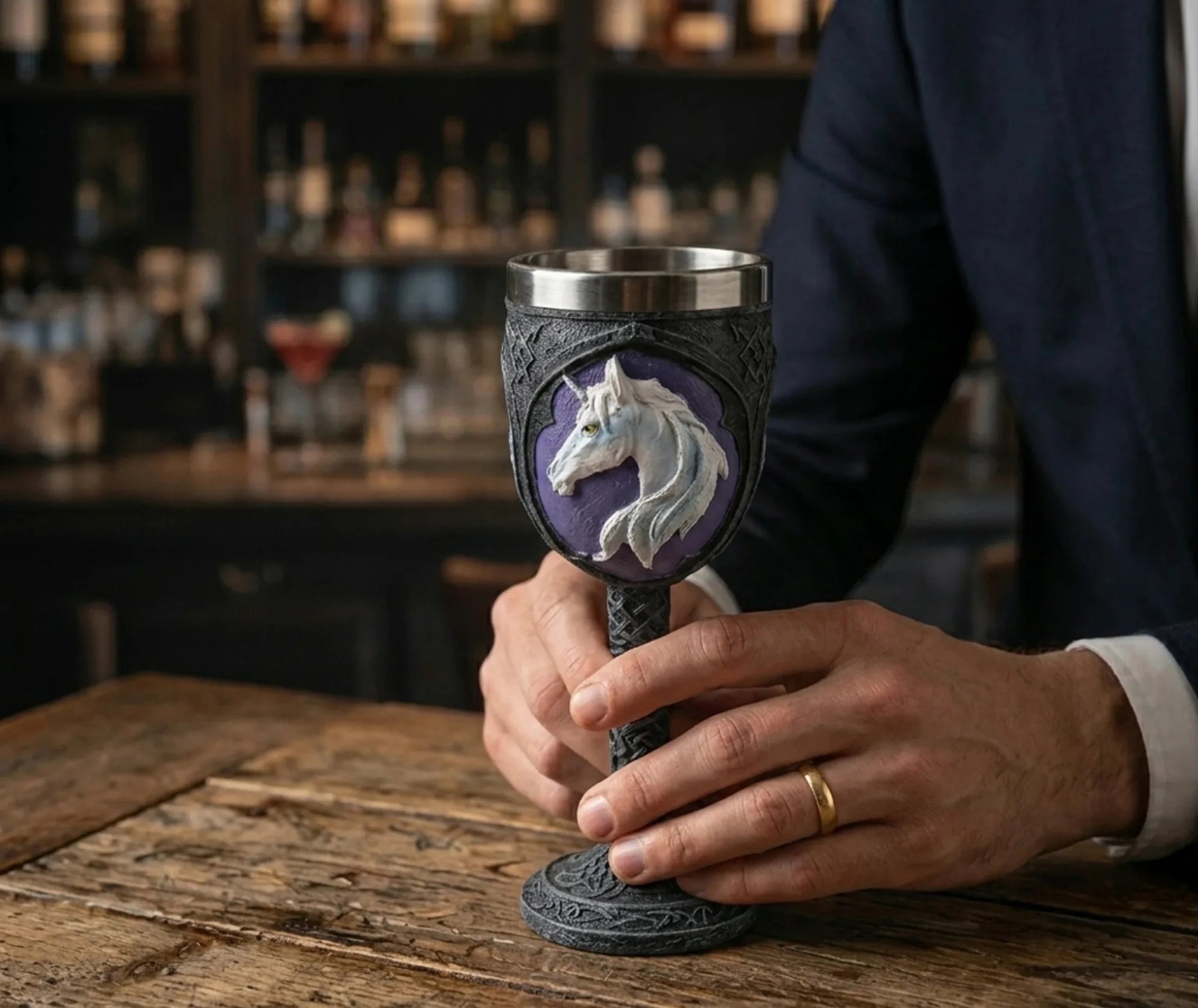 Une main tenant le calice Licorne posé sur le comptoir d'un bar, bouteilles en arrière-plan