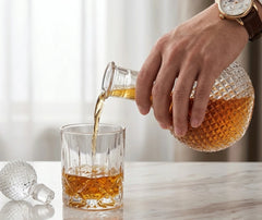 Whisky versé depuis la carafe ancienne dans un verre en cristal taillé, sur une table en marbre.