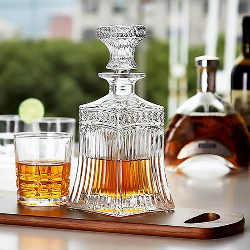 Carafe à whisky en cristal vintage sur une planche en bois en terrasse, avec un verre garni d'une rondelle de citron vert et vue sur la ville en arrière-plan.