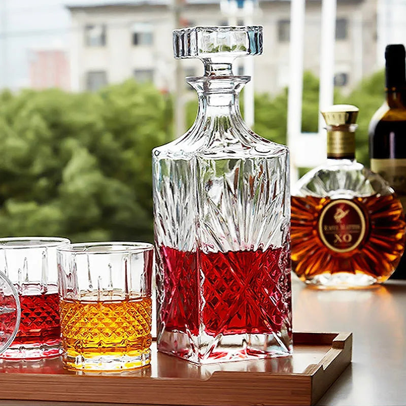 Carafe à whisky en cristal remplie de liqueur rouge et deux verres sur un plateau en bois en terrasse, avec vue sur la ville en arrière-plan