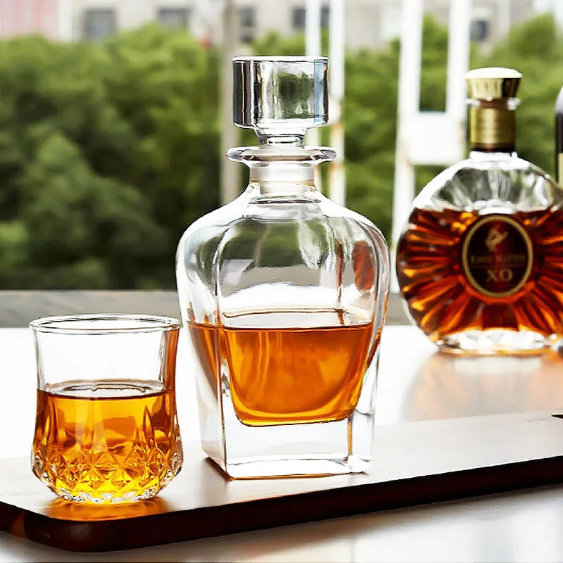 Carafe à whisky et verre rempli sur une table extérieure, avec une bouteille de cognac XO en arrière-plan et de la verdure floutée.
