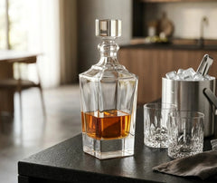 Carafe à whisky américaine posée sur un plan de travail noir dans une cuisine moderne, entourée de deux verres à whisky ciselés et d'un seau à glace.