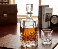 Carafe en cristal remplie de whisky posée sur un bureau en cuir, à côté d'un verre assorti, d'une mallette et d'une horloge.