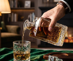 Un homme verse du whisky depuis la carafe en cristal dans un verre assorti, sur un plateau en velours vert dans un salon cosy.