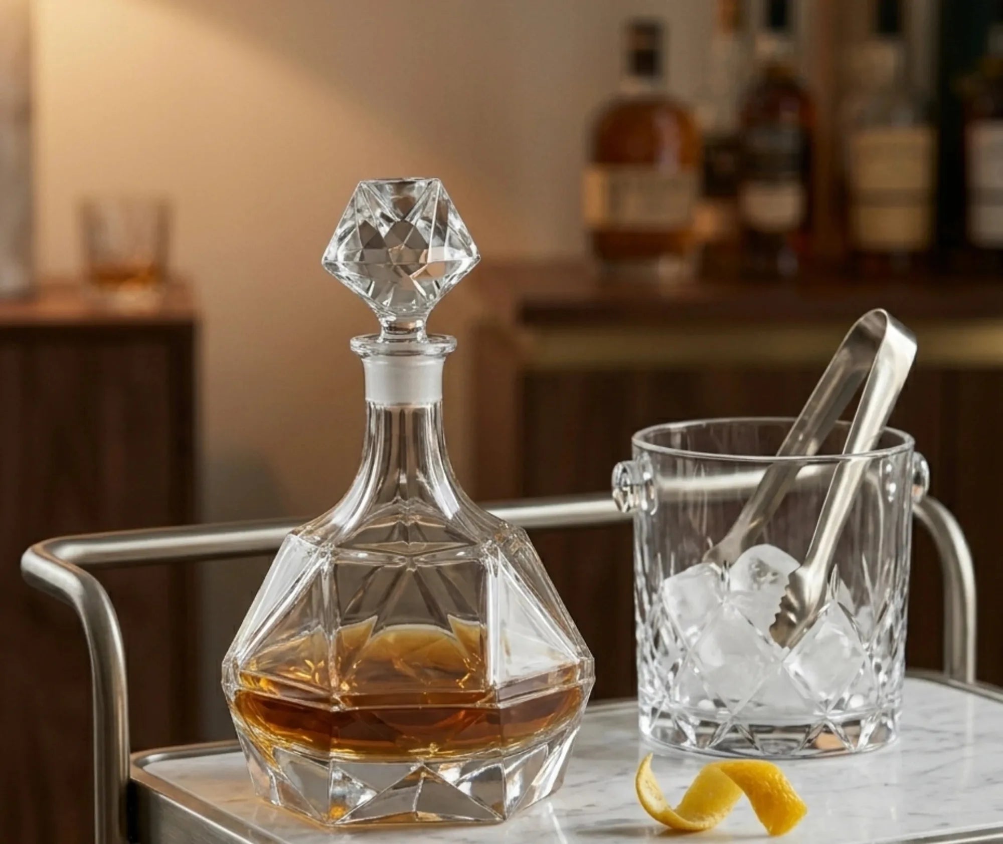 Carafe à whisky en cristal sur un chariot de bar, à côté d'un seau à glace avec pince et d'un zeste de citron, ambiance bar chaleureuse.