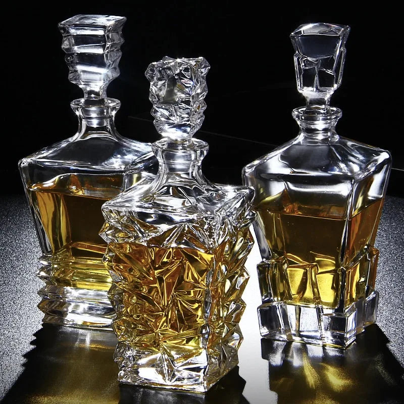 Trois carafes à whisky en cristal aux designs différents, remplies d'alcool ambré, posées sur fond noir avec reflets dorés.