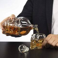 Gros plan sur le filet de whisky ambré coulant de la carafe tête de mort dans le verre crâne assorti