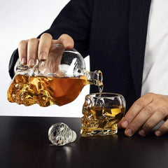 Un homme en costume verse le whisky de la carafe tête de mort dans un verre à whisky en forme de crâne assorti, bouchon en diamant posé sur la table