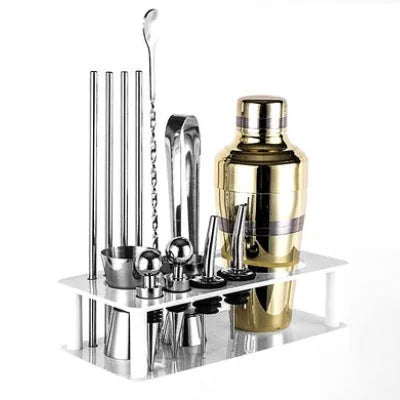 Shaker doré et accessoires en inox du coffret cocktail installés sur leur support de rangement blanc.