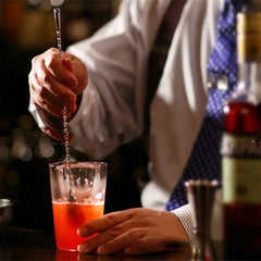 Barman utilisant la cuillère à cocktail grande taille pour préparer un cocktail rouge