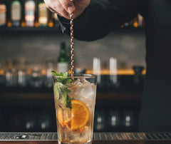 Cuillère à cocktail torsadée plongée dans un mojito garni de menthe fraîche et d'une rondelle d'orange.