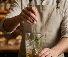 Barman utilisant la cuillère de bar torsadée pour remuer un cocktail glacé garni de feuilles de menthe fraîche.