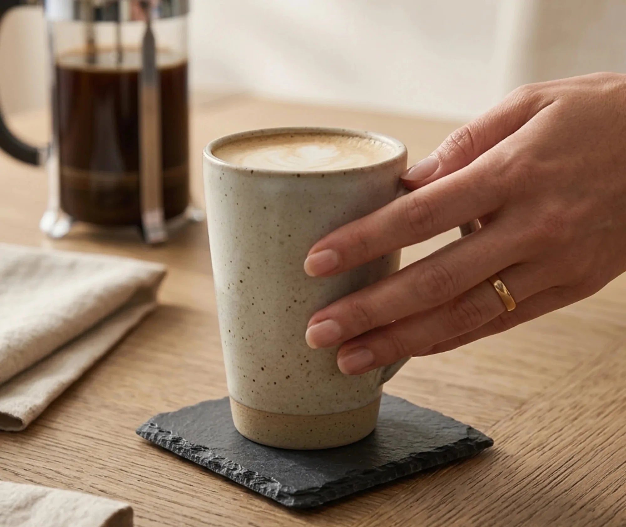 Dessous de verre en ardoise posé sur une table en bois sous une tasse de café tenue à la main