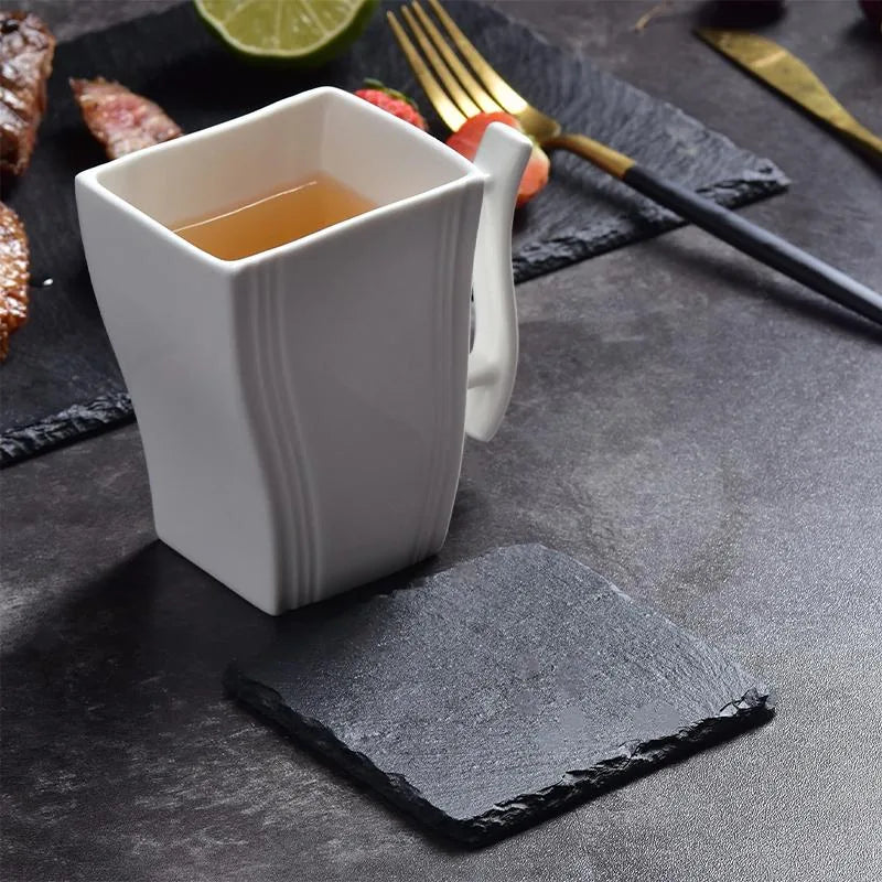 Dessous de verre en ardoise sous une tasse de thé accompagnée de fraises et de viande grillée sur table sombre
