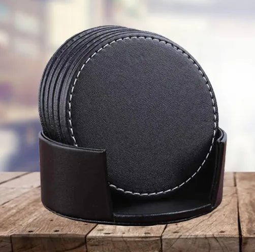 Lot de 6 dessous de verre en cuir noir empilés dans leur boîtier de rangement, posés sur une table en bois.