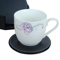 Tasse en porcelaine à motif floral posée sur un dessous de verre en cuir noir, à côté du boîtier de rangement.