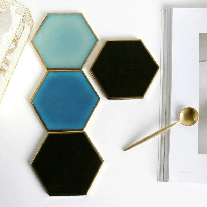 Assortiment de quatre dessous de verre hexagonaux en dégradé de bleu et de noir, posés en colonne à côté d'un magazine et d'une cuillère dorée.